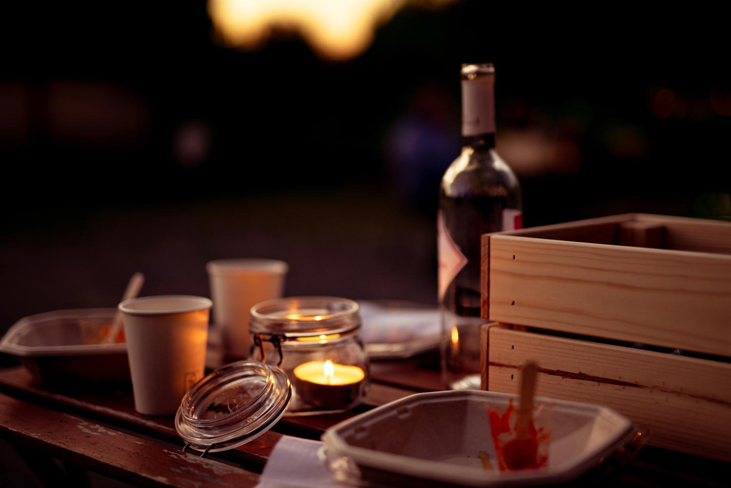 An outdoor table with candle and empty plates and empty bottle of wine